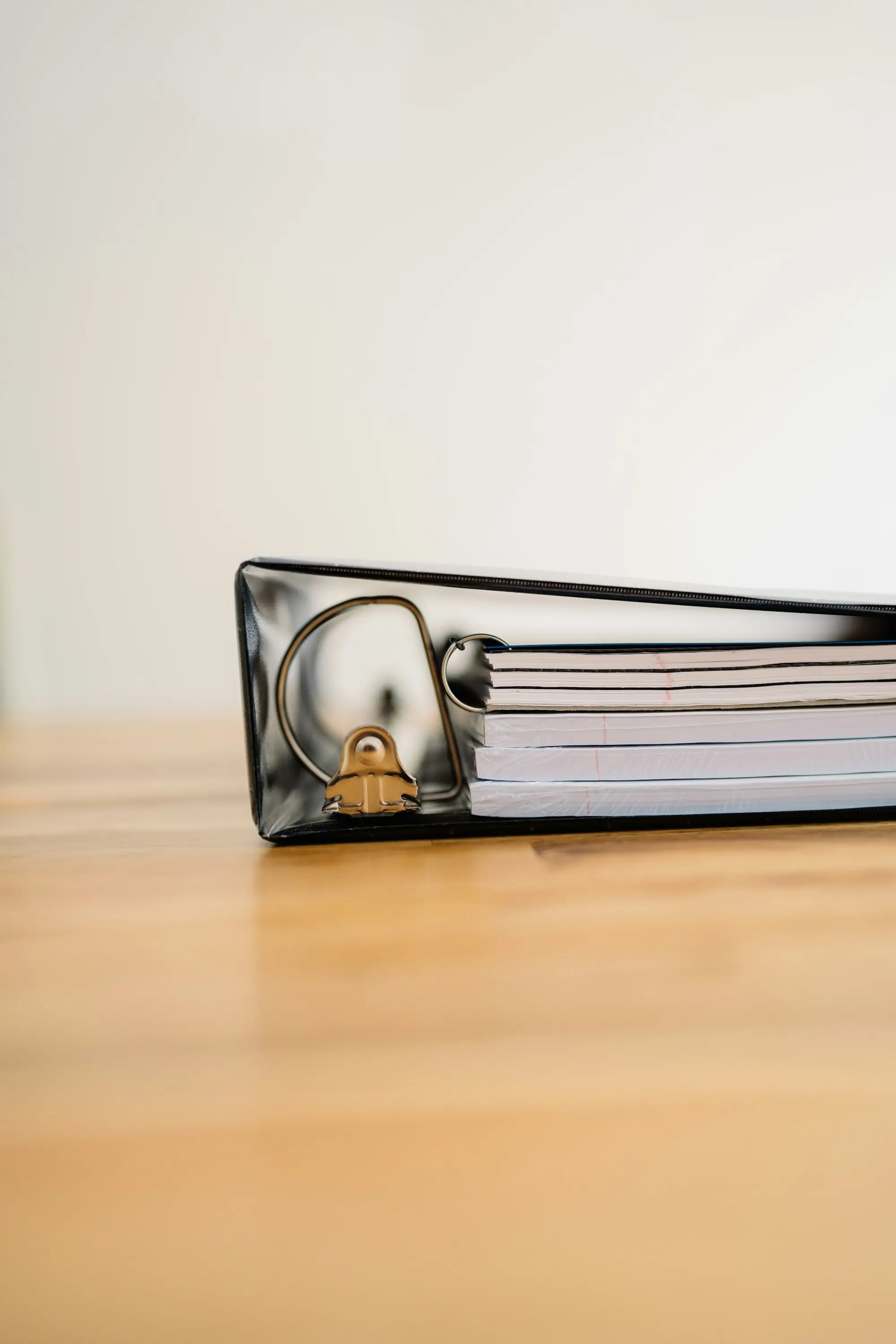 Close-up of a ring binder full of papers resting on a wooden desk.