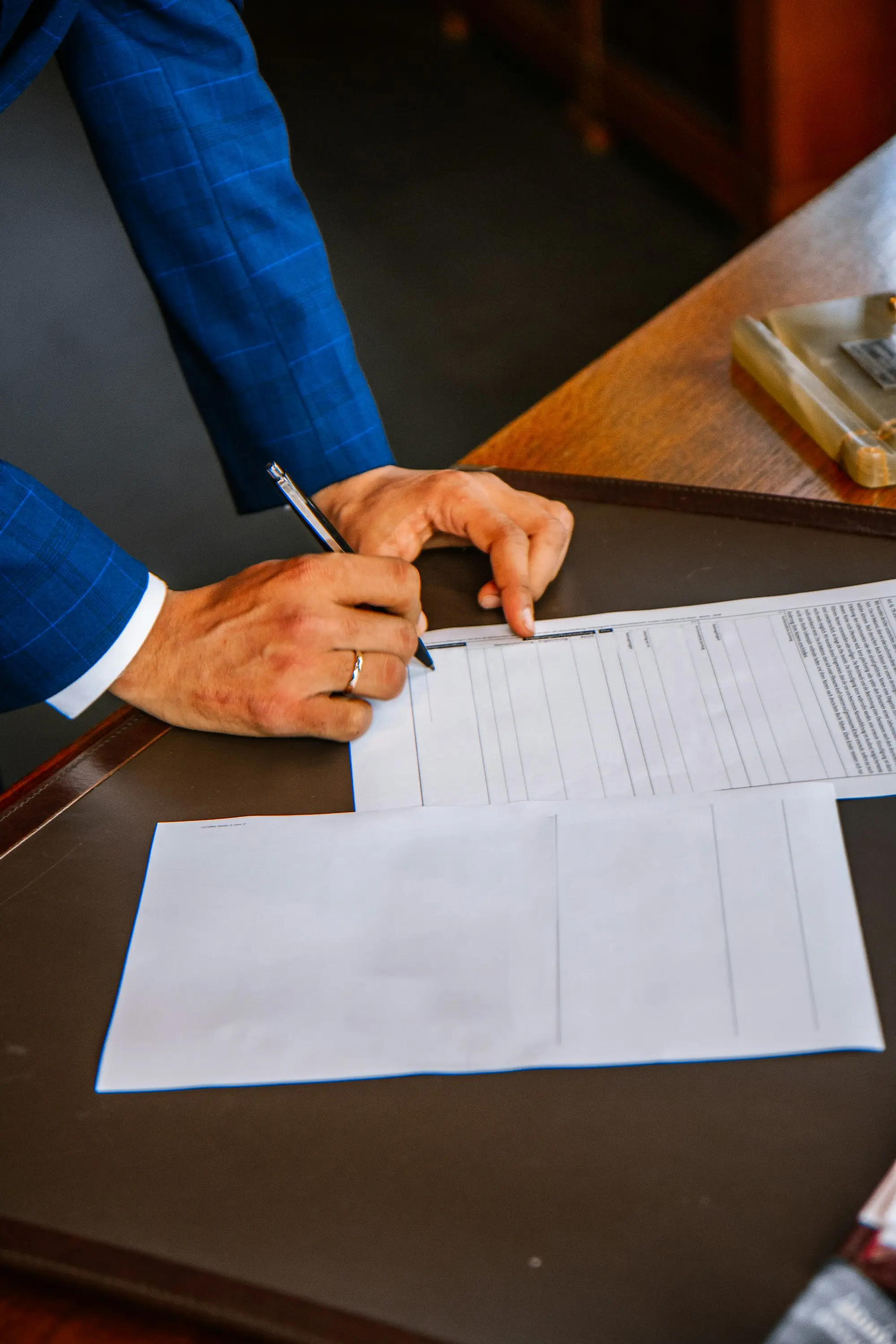 Hands signing a document with a pen at a desk, papers laid out in front of the signer.